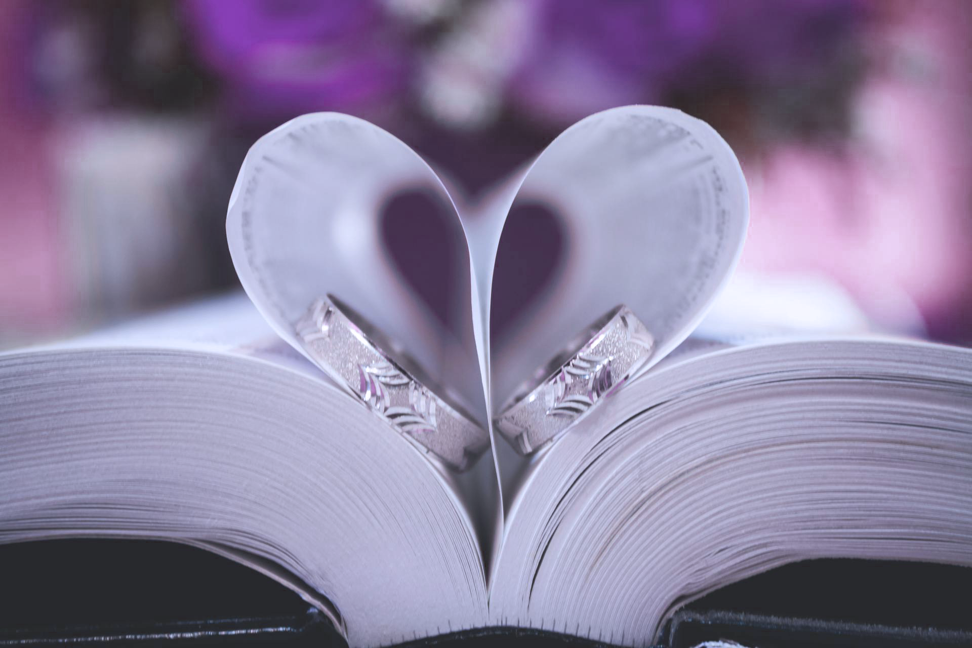 Photo livre ouvert avec pages en forme de coeur et alliances au milieu